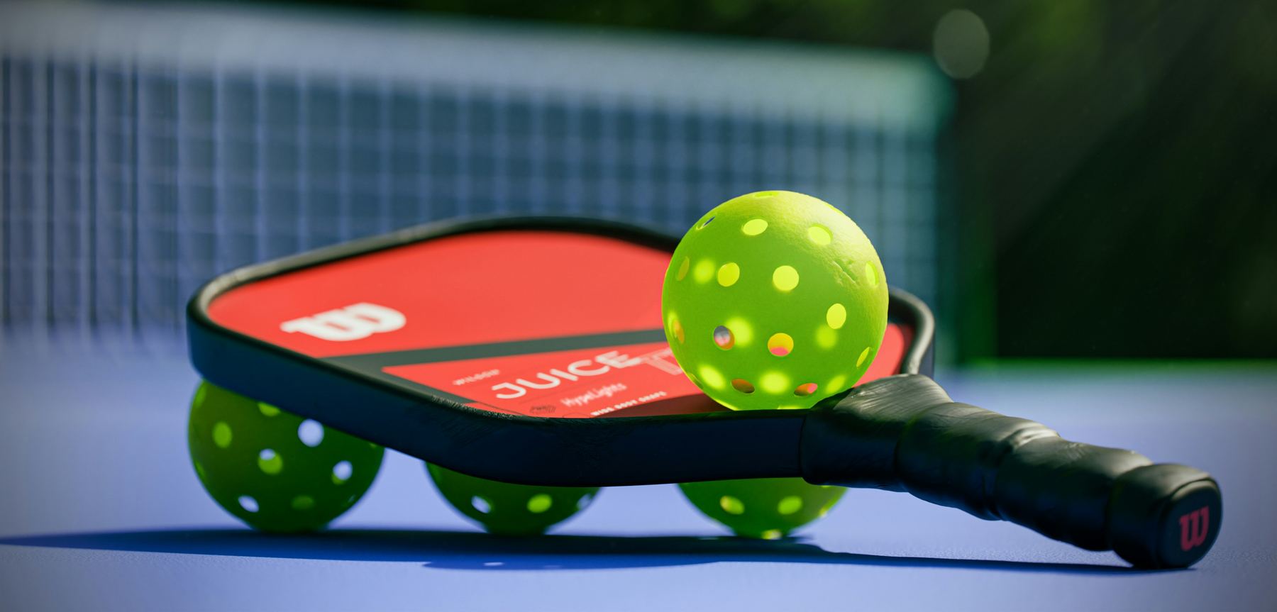 A pickleball paddle and balls resting on a court beside the net